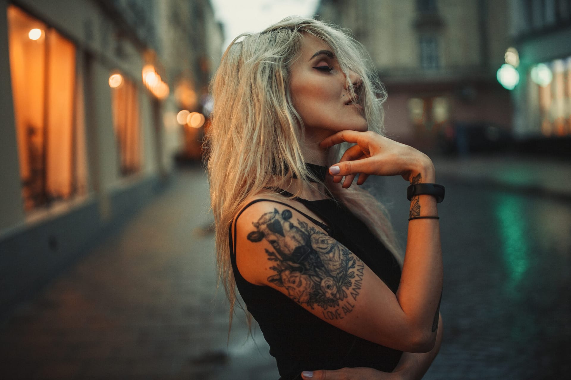 Young woman portrait with tattoo on shoulder standing on city street in evening. In background there are city lights.