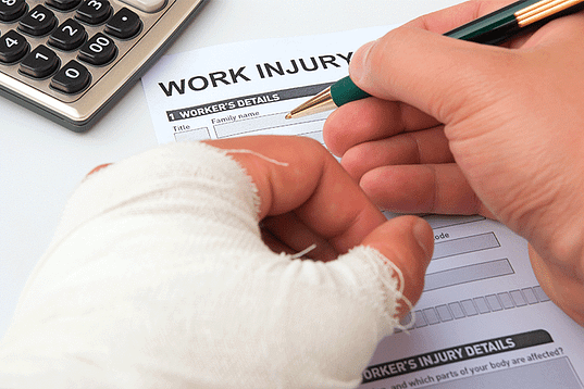 Man with bandaged hand filling out a work injury form - Dallas workers' compensation attorneys in DFW, Texas