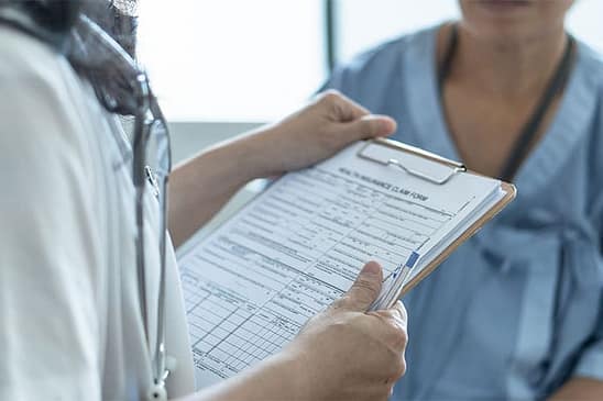 La guía esencial de PIP vs Med Pay 2 Un médico con un portapapeles hablando con un paciente. ¿Cuál es la diferencia entre la protección contra lesiones personales y la cobertura de pagos médicos al presentar una reclamación por lesiones personales?