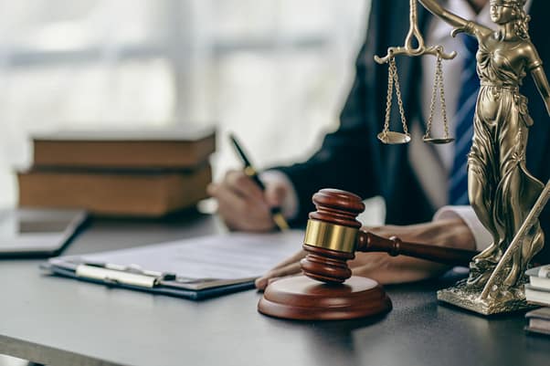 3 elementos clave que determinan la culpa en un accidente automovilístico en Texas 4 Man sitting at a desk reviewing paperwork with Lady Justice on the table next to a gavel.