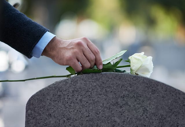 Man placing a white rose flower on a grave - Survival action lawyers in Texas