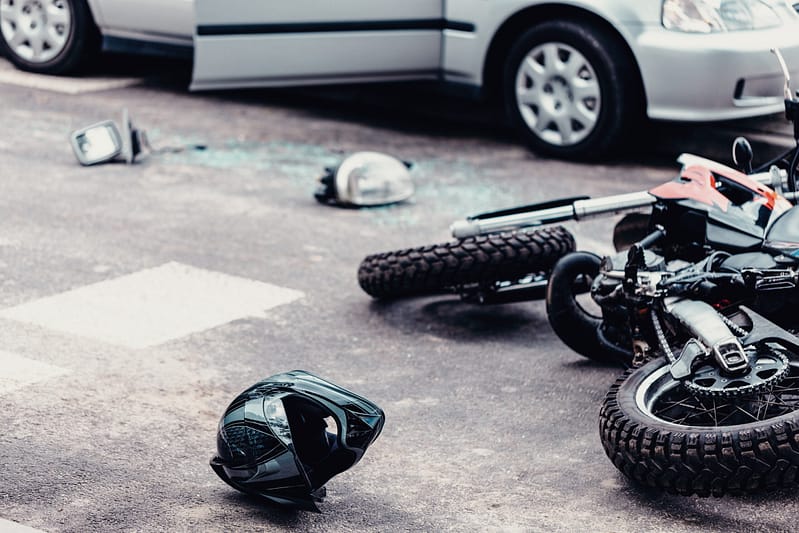 Helmet and motorcycle next to broken pieces of a car on the street after car crash. Injuries motorcycle accidents. El Paso Motorcycle Accident Lawyers